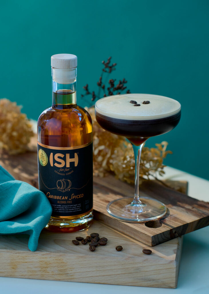Butelka bezalkoholowego ISH Caribbean Spiced i espresso martini z ziarnami kawy na desce z naturalnego drewna