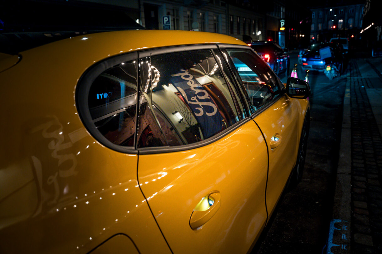 Żółty samochód nocą w centrum miasta, odbijający w szybie logo Ford i światła uliczne - zdjęcie w stylu lifestyle, idealnie wpisujące się w atmosferę premium drinków bezalkoholowych Trendy Taste i ISH Spirits.