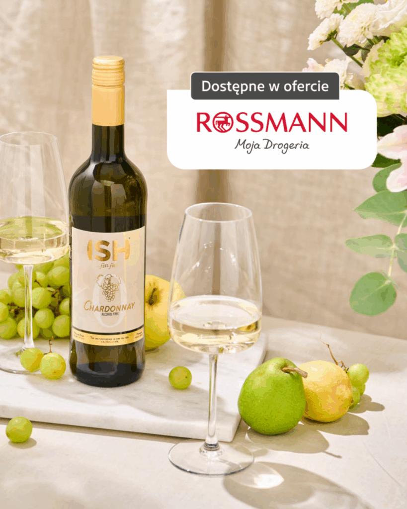Butelka bezalkoholowego ISH Chardonnay na stole z winogronami, gruszką i cytryną, dostępna w ofercie Rossmann.