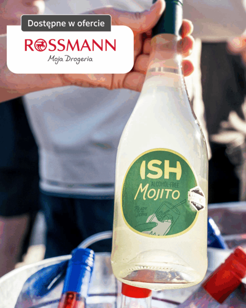 Butelka bezalkoholowego ISH Mojito trzymana w dłoni, dostępna w ofercie Rossmann, w otoczeniu imprezowej plenerowej scenerii.