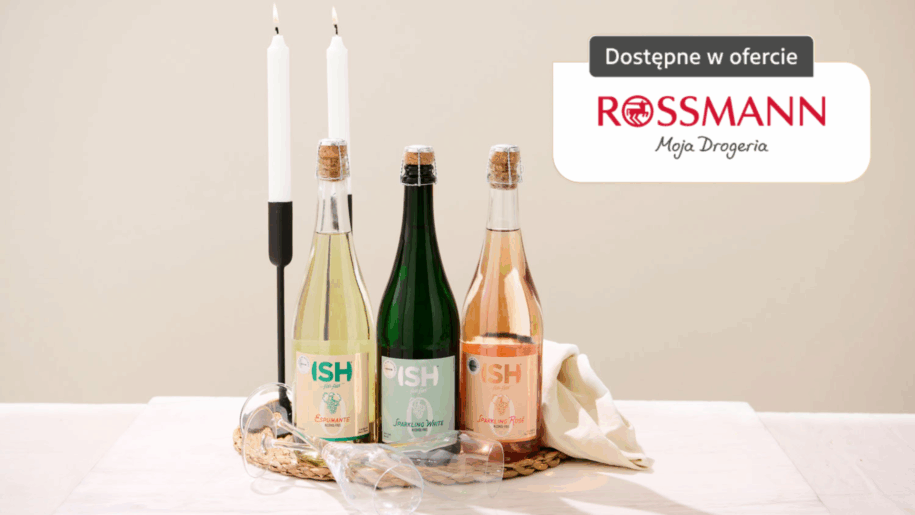 Trzy bezalkoholowe wina musujące ISH dostępne w Rossmann, ustawione na stole w eleganckiej aranżacji z kieliszkami i świecami.